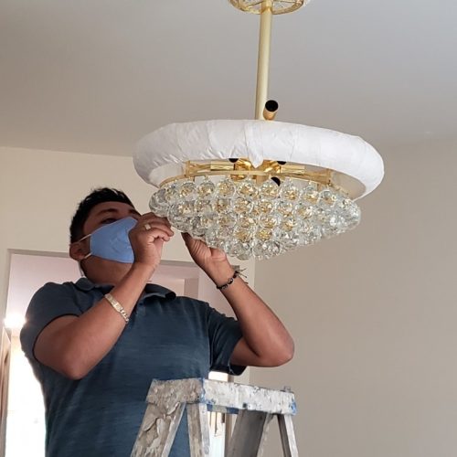 a man in blue shirt fixing a bulb on a chandelier