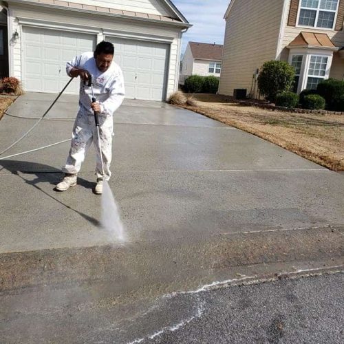 a man in uniform pressure washing a driveway garage