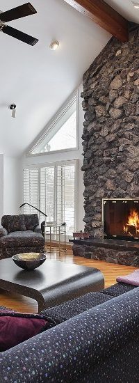 A cozy living room with a fireplace, comfortable sofa, and a large window overlooking a snowy landscape.